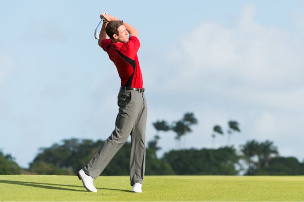 Mann führt einen Golfschwung auf einem Golfplatz aus – dynamische Drehbewegung im Oberkörper.